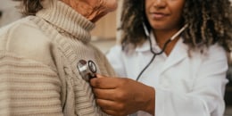 Healthcare professional listening to elderly woman's heart with stethoscope at home - home consultation.