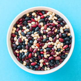 Mix of raw beans in a white bowl on a blue background. Top view and copy space.