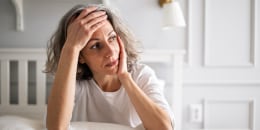 Mature woman lying on bed, expressing negative emotions silently.